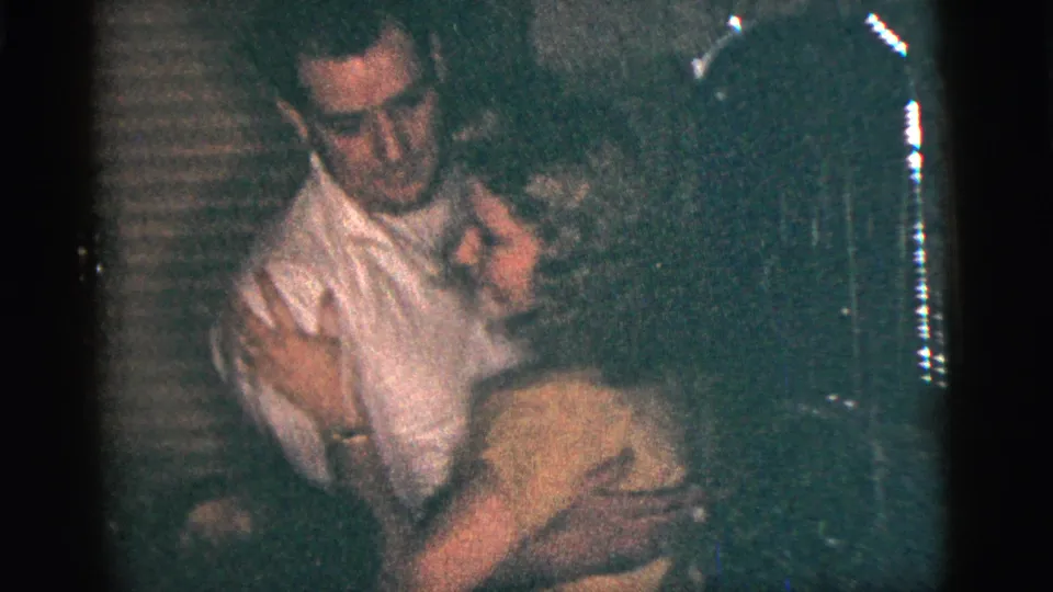 1956 New York City home-movie frame showing the couple mid-dance, held close in a dim private interior.