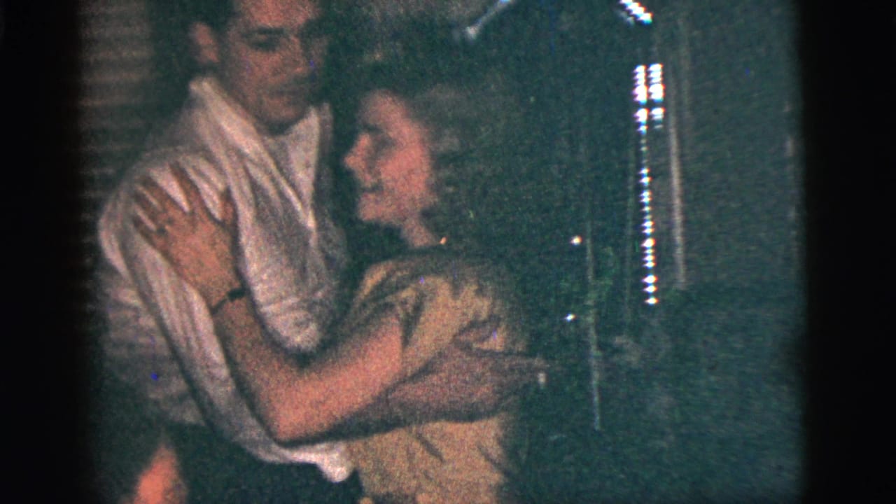 Young man and woman dance closely in a dim room.