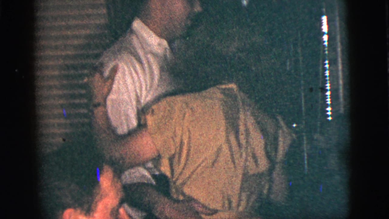 Man in a white shirt embraces a woman while dancing in a dark room.