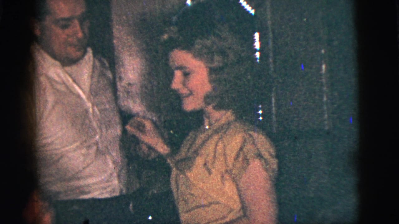 In 1956 New York City home-movie footage, a man in a white shirt and a woman in a light dress dance in a dark indoor gathering.