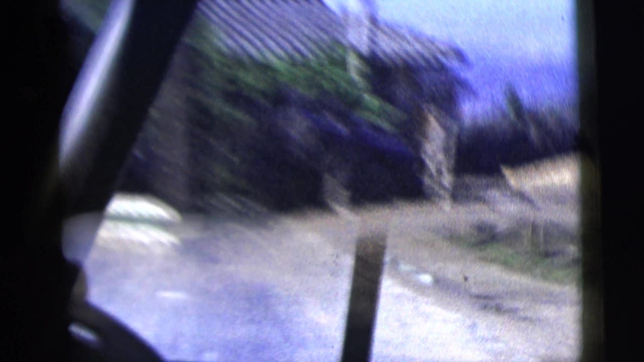 Road and roadside wall seen through a dark car-window frame during a moving drive.
