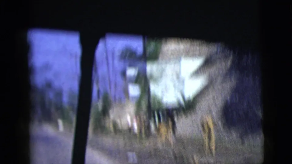 A 1958 car-passenger view shows a paved road, white roadside building, posts, vegetation, and heavy motion blur.