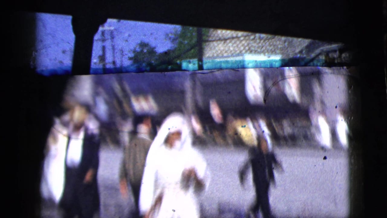 1958 New York City home-movie frame showing blurred pedestrians on a street, viewed through a dark vehicle window or frame edge.