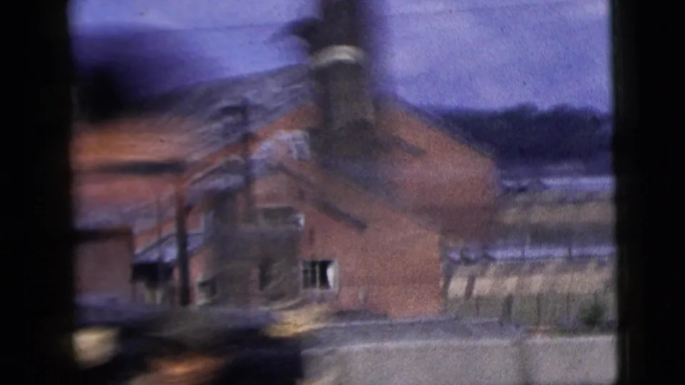 1958 New York City drive-by frame showing a brick building with a sloped roof, roadside structures, and strong motion blur.