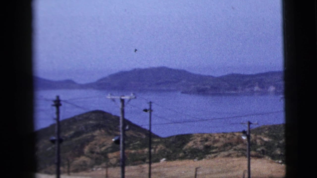 1958 8mm view of calm water, distant hills, and foreground power lines from a framed roadside or window perspective.