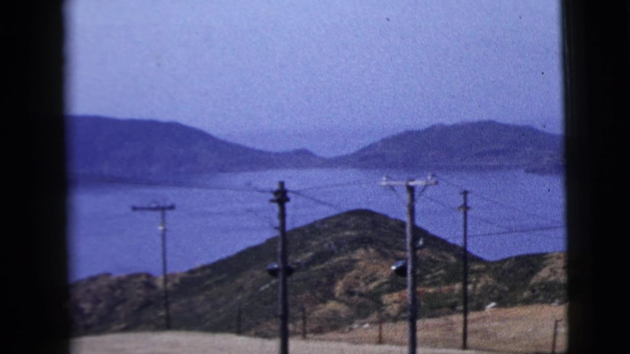 Rolling hills, water, and utility poles viewed through a dark vertical frame.