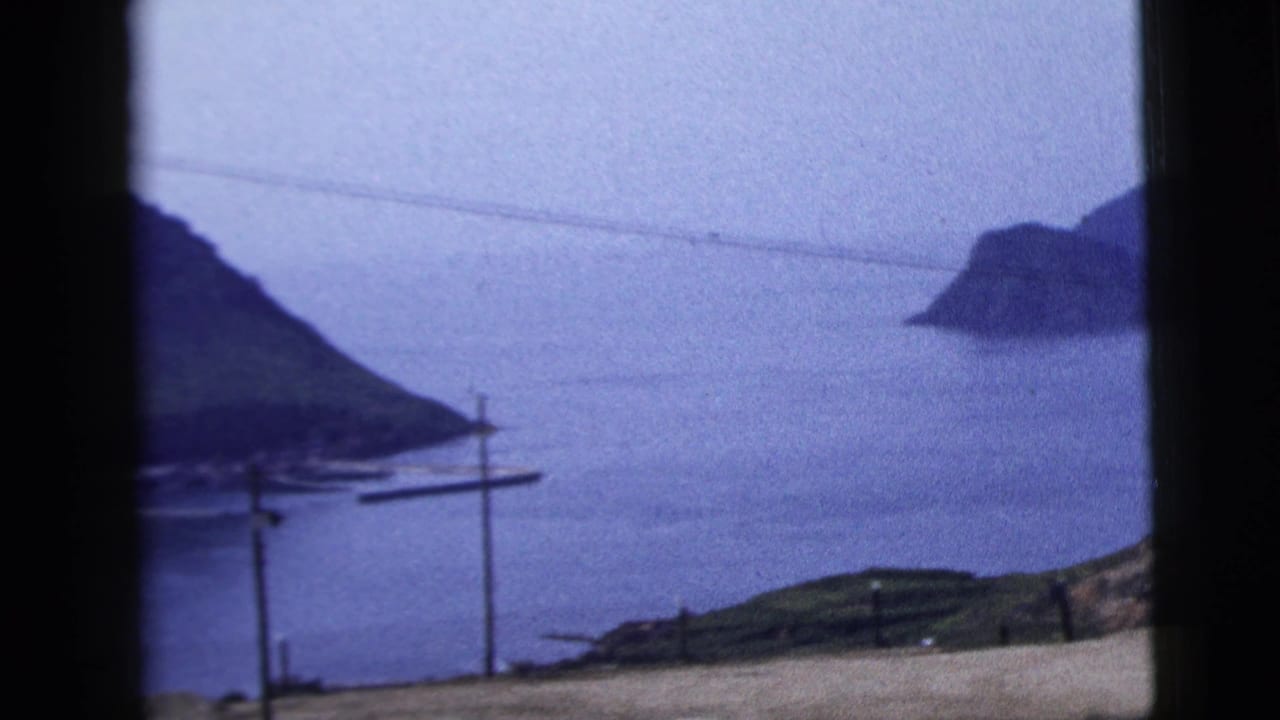 1958 8mm home-movie view of a calm harbor, distant landforms and utility poles framed by a dark vehicle or window edge.