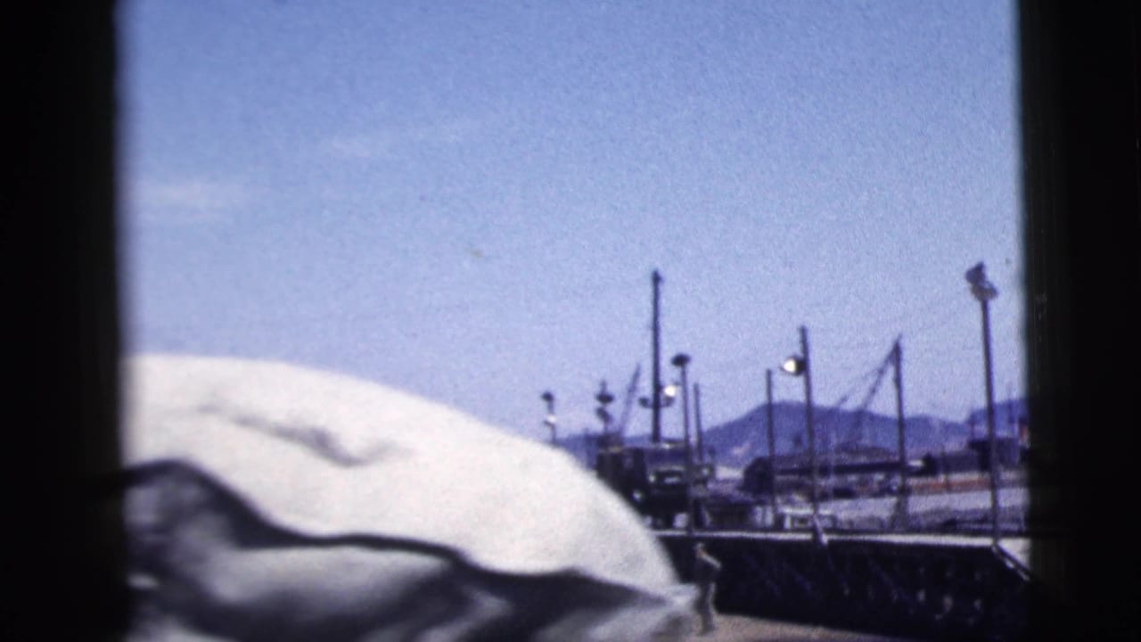 Covered object and dock structures beside a vessel under a bright blue sky.