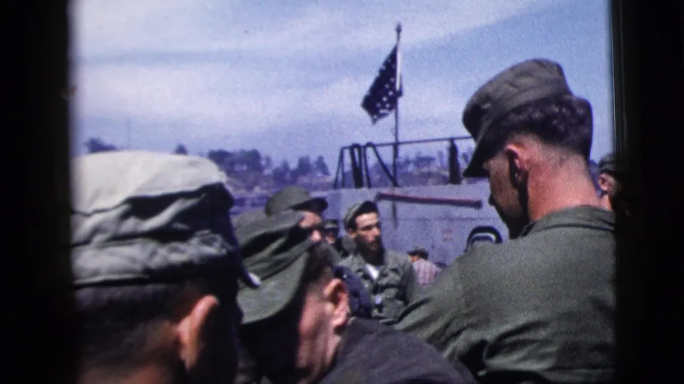 Close 8mm view of soldiers at a New York City port in 1958, with caps, ship railings, a flag, and waterfront background visible.