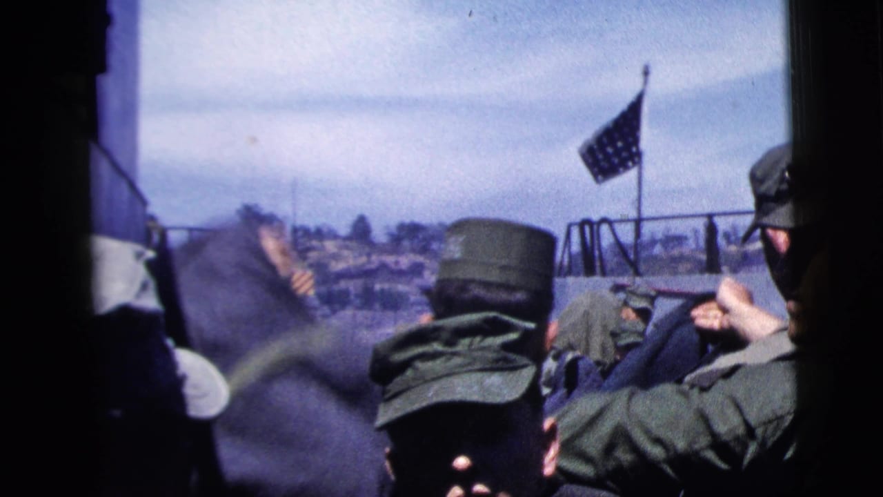 Uniformed men on a ship deck are partially obscured by dark framing, with an American flag and harbor shoreline visible behind them.