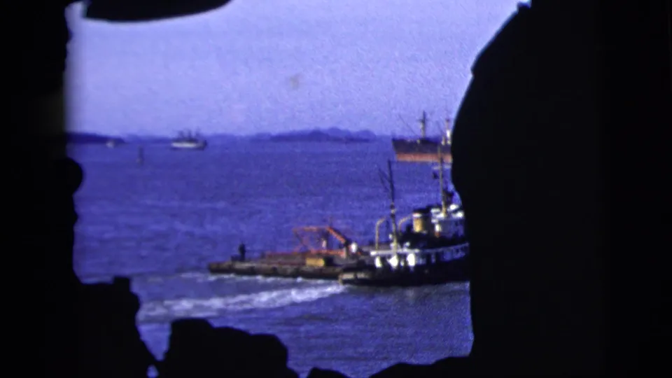 The harbor view shows a tugboat, distant ships, blue water, and dark shipboard edges framing the scene in 1958 New York City footage.