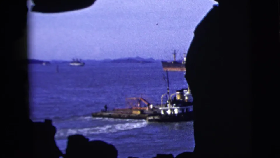 1958 New York City harbor view with small boats and distant vessels framed by dark foreground silhouettes.