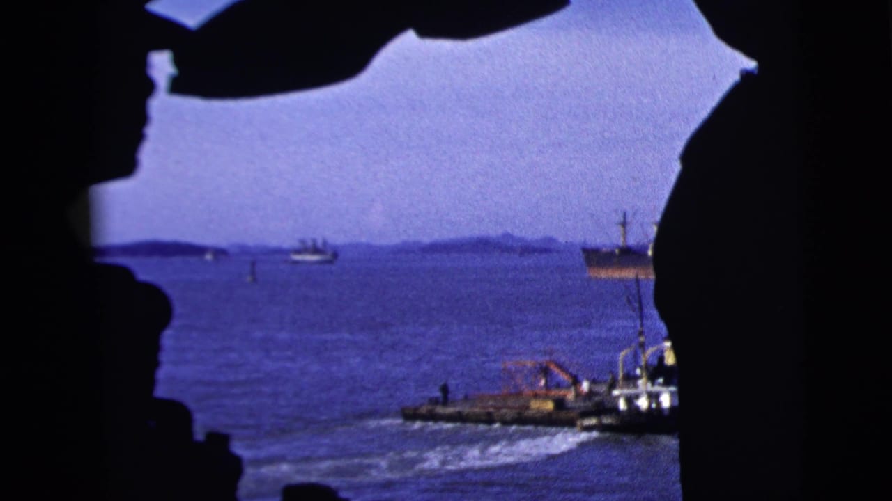 A small workboat passes on blue water with a larger vessel in the distance.