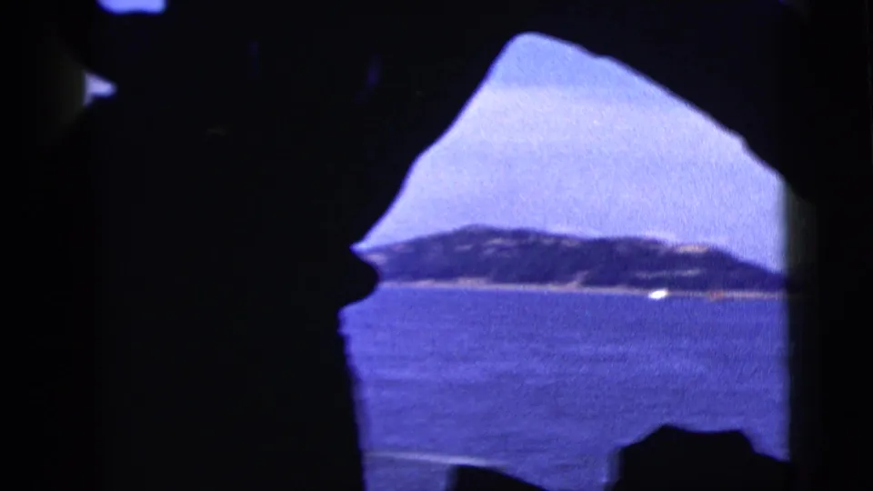 A blue-tinted 1958 harbor view in New York City, looking past dark foreground silhouettes toward a low shoreline.