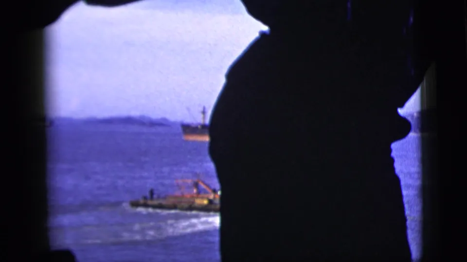 1958 New York City 8mm frame looking through a window past a dark hat silhouette toward boats on a calm bay.