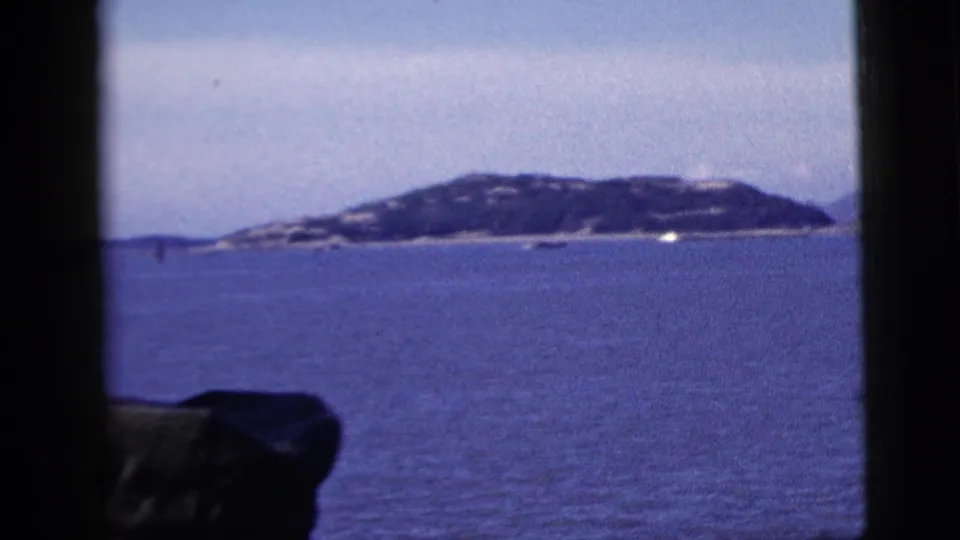 A 1958 New York City harbor view holds on open water and distant land while a foreground hat remains at the lower edge.