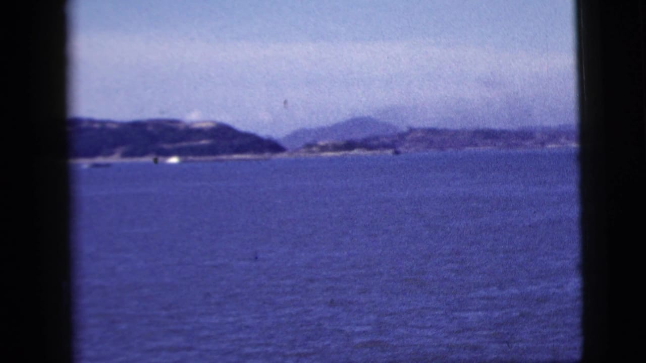 Blue water and a hazy coastline appear through the vessel window, with small boats scattered near the horizon in 1958 New York City footage.