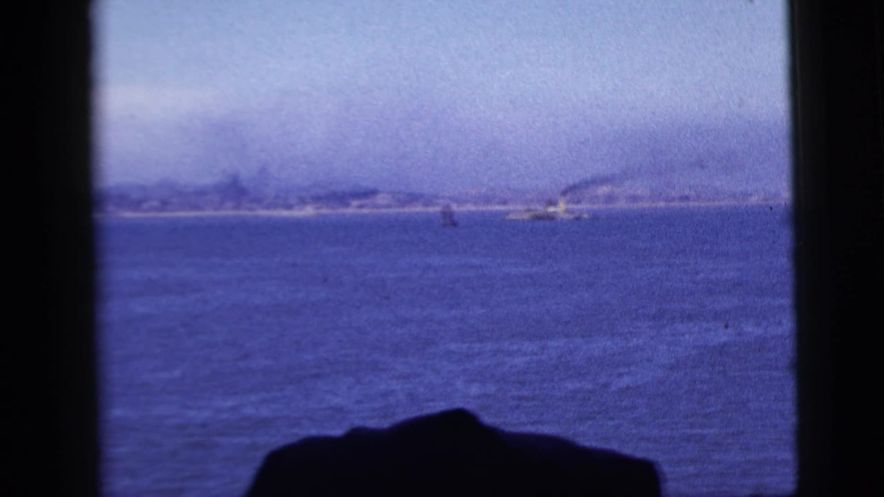 Ocean view through dark window framing with distant shoreline under a hazy sky.