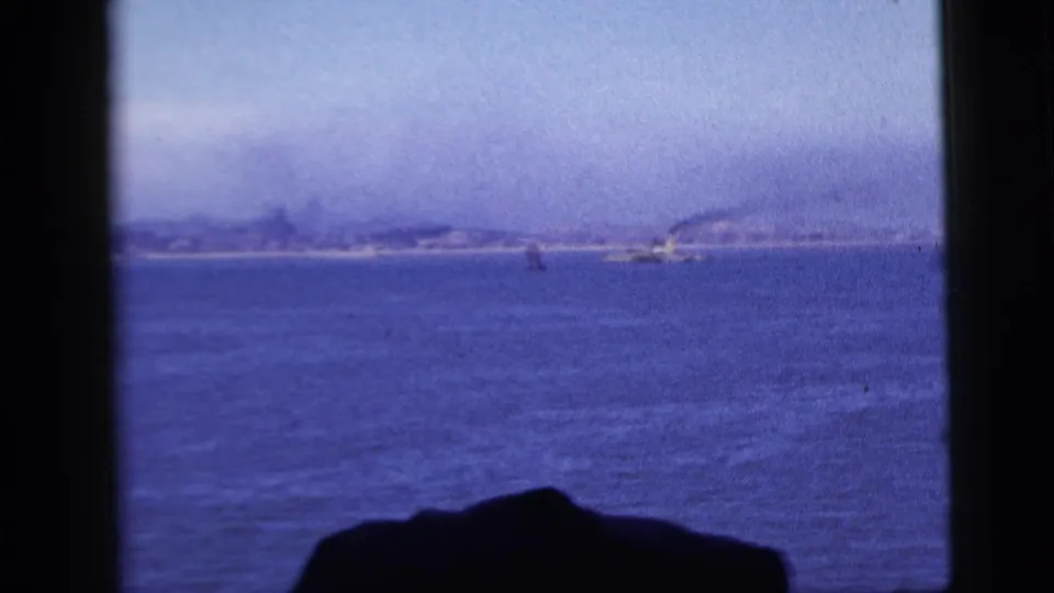 1958 New York City-area 8mm view across blue water toward a hazy distant shoreline, framed by dark vessel-window edges.