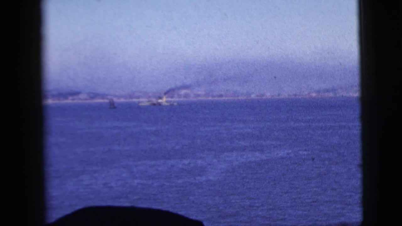 Distant coast and small boat shapes across blue water, bordered by a dark window frame.