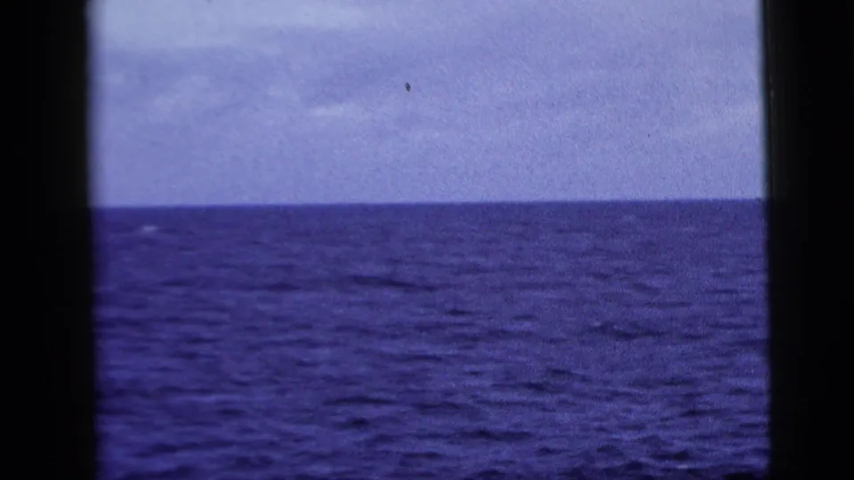 1958 8mm ocean view from a moving vessel, showing textured blue water, pale sky, and dark framing at the edge of the shot.