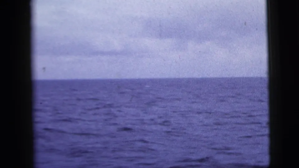 1958 8mm home-movie still of blue ocean under low cloud, partly interrupted by dark window-like framing.