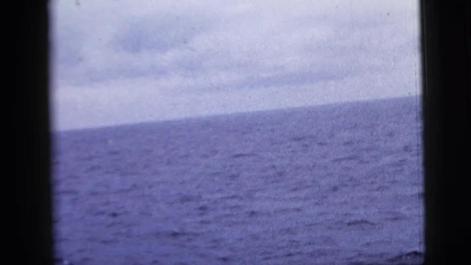 1958 8mm frame with a slightly tilted ocean horizon, cloudy sky, and dark framing along the center and sides.
