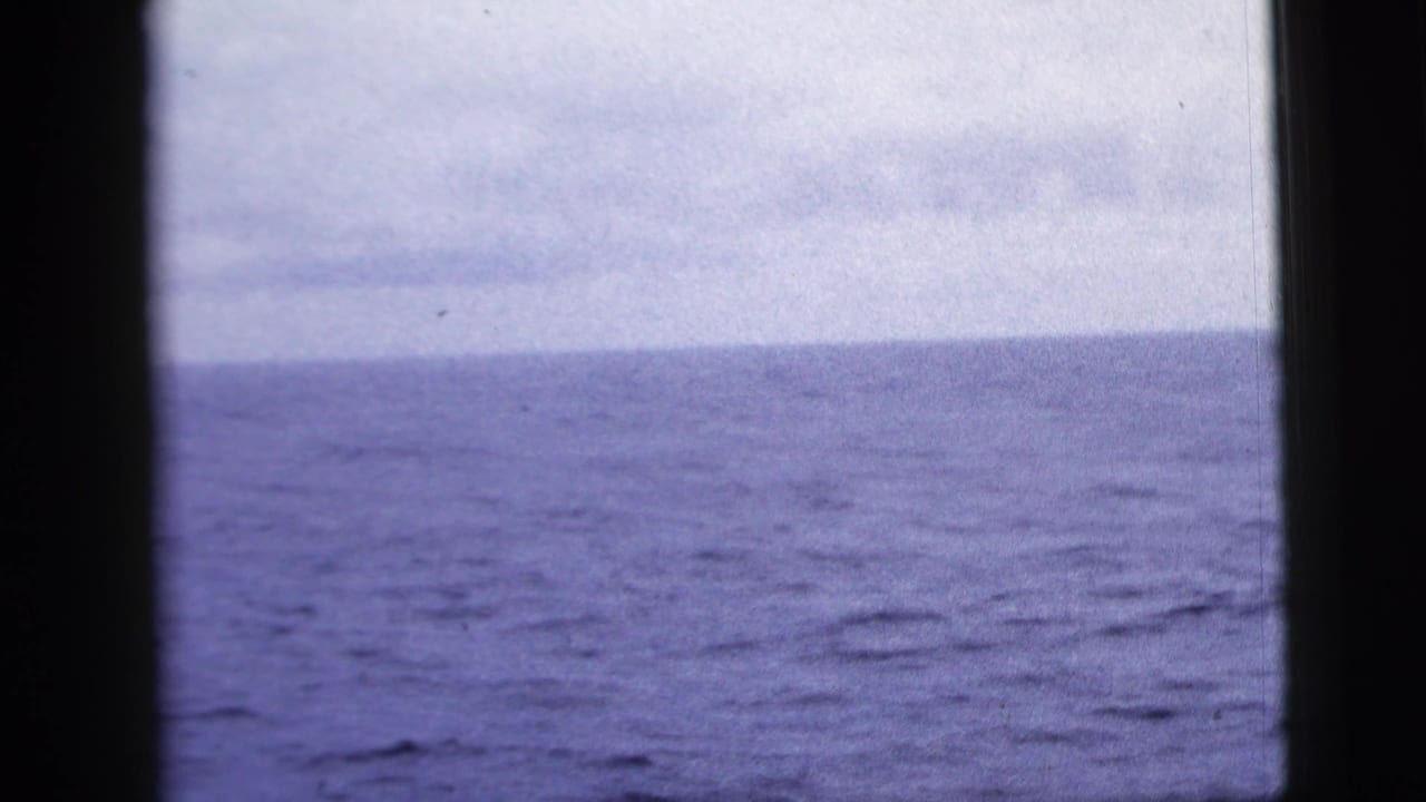 1958 8mm home-movie frame showing blue-gray ocean and overcast sky through dark ship window framing.