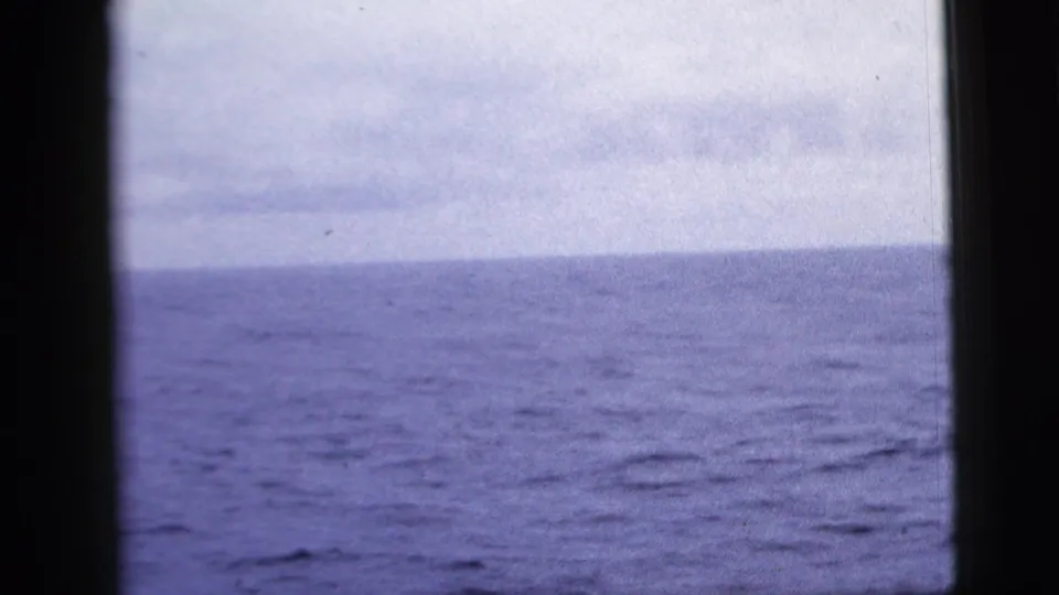 1958 8mm home-movie frame showing blue-gray ocean and overcast sky through dark ship window framing.