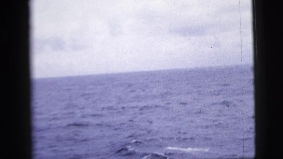 1958 shipboard ocean view with a low horizon, overcast sky, and dark window structure crossing the frame.