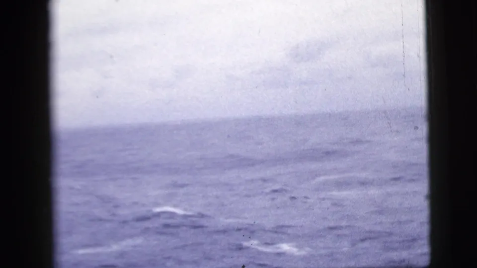 1958 8mm frame of a soft blue-gray sea and pale overcast sky from a shipboard passenger viewpoint.