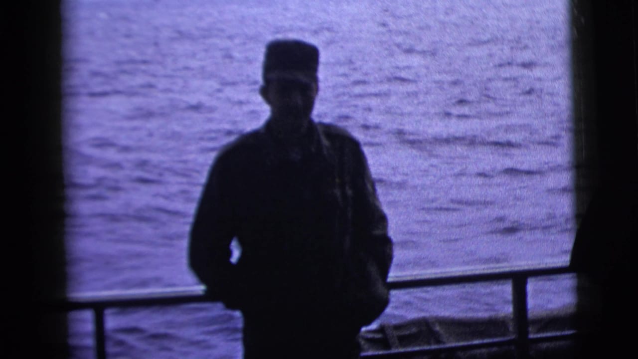 A silhouetted adult man in military-style dress stands by a boat railing against the ocean in 1958 New York City home-movie footage.