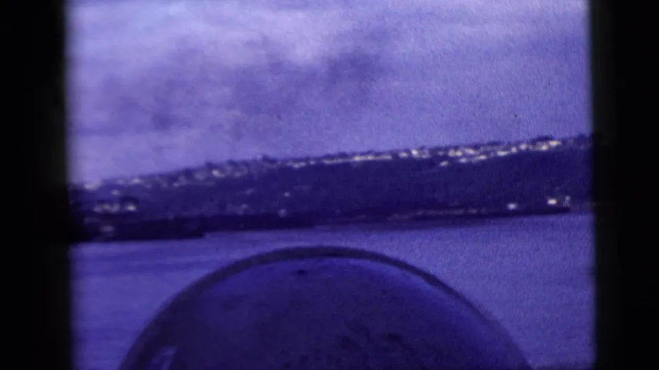 Blue-shifted 8mm frame of a distant New York City shoreline, with a rounded foreground object suggesting filming from a vessel.