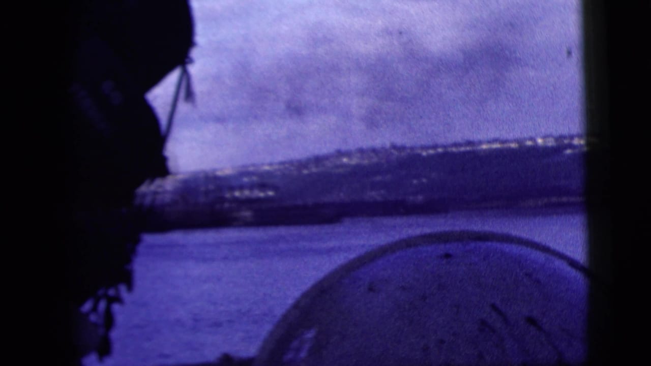 1958 8mm New York City harbor view from a vessel window, with dark framing, water, distant shoreline, and a partial foreground silhouette.