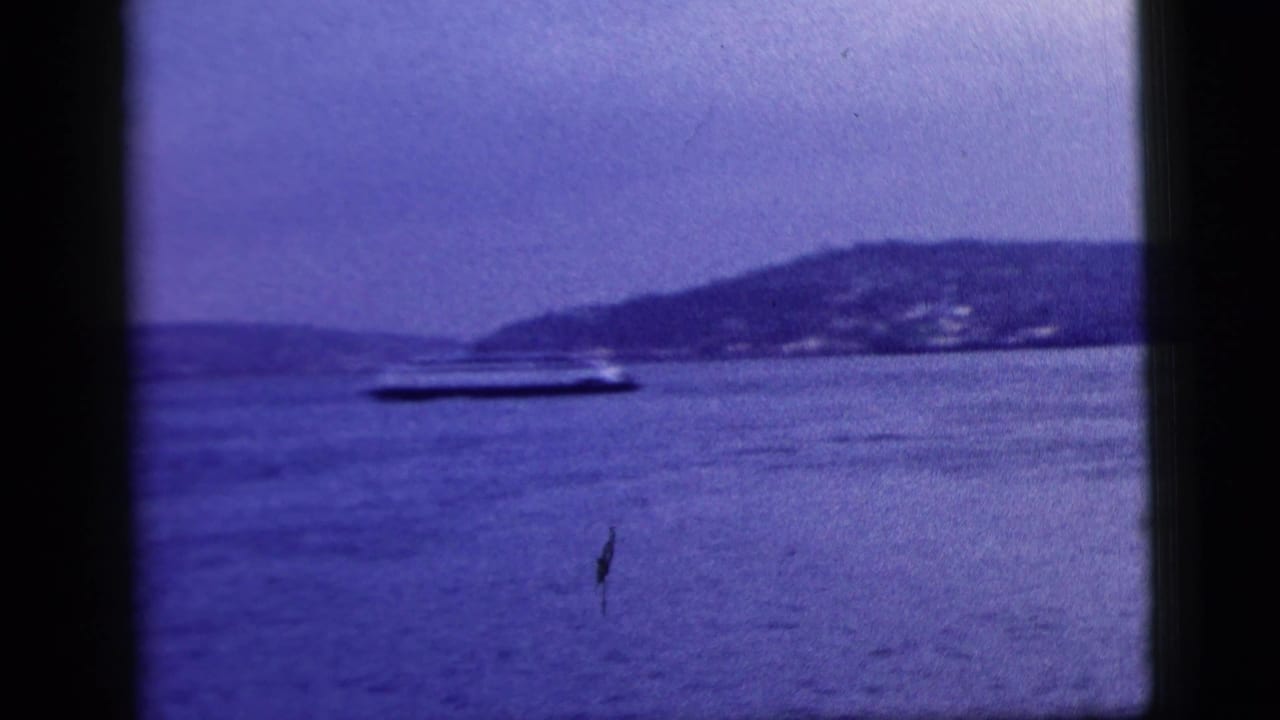 Small boat crossing open water with a hilly shoreline in the distance.