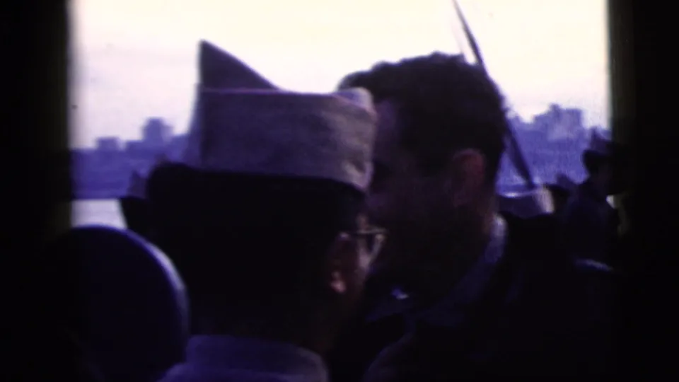 1958 New York City home-movie frame with soldiers and civilians in silhouette watching a distant skyline across the river.