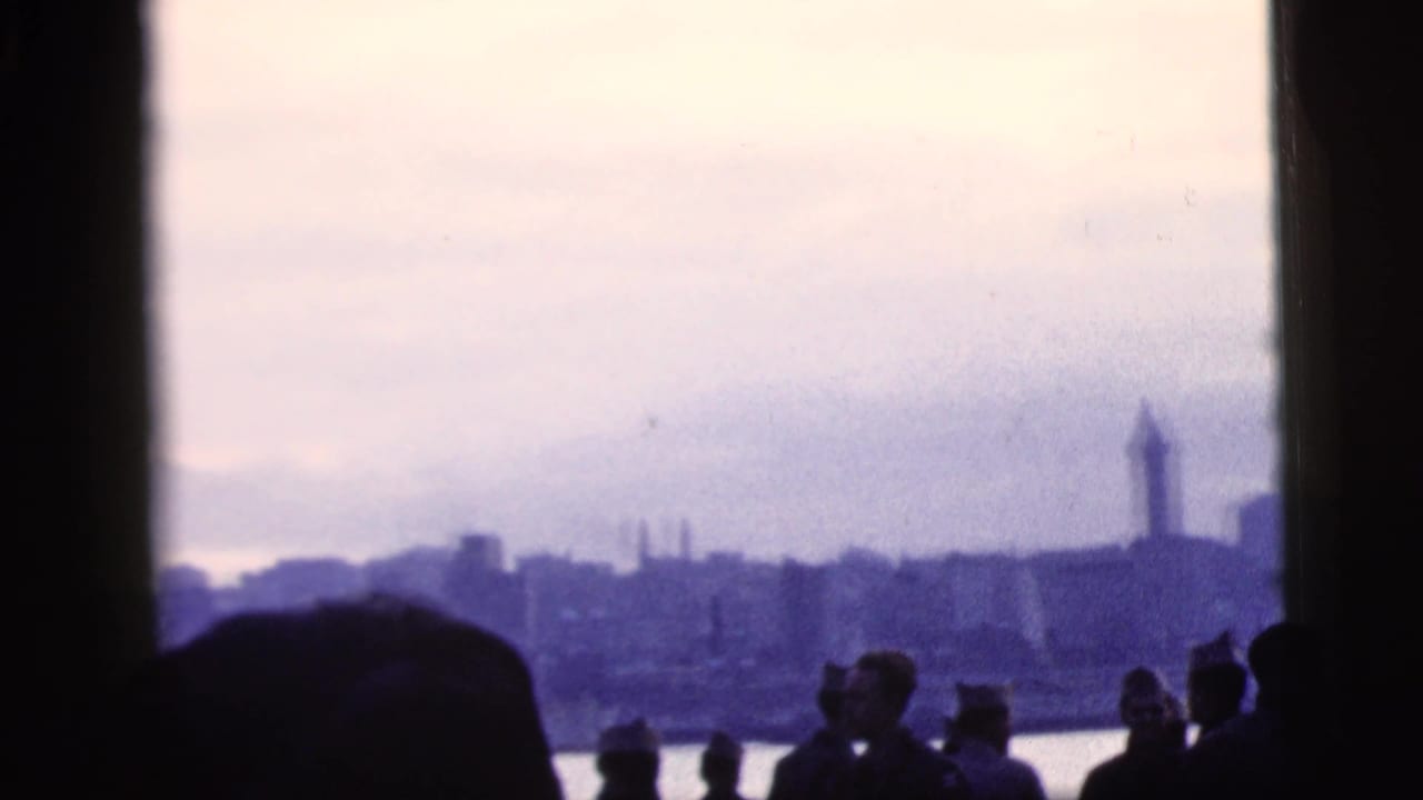 New York City river view from the boat, with passenger silhouettes in the foreground and a tower-like structure on the skyline.