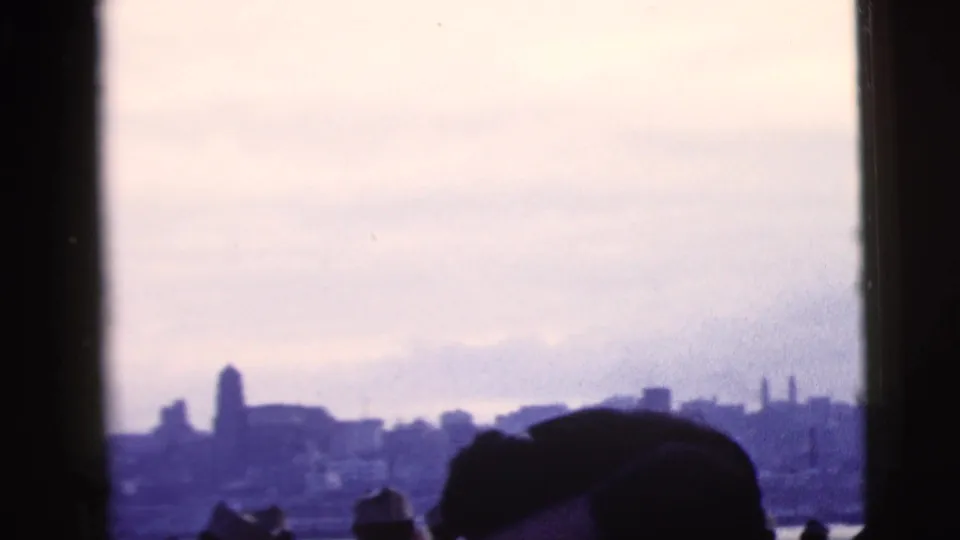 Home-movie view of passengers looking toward the New York City skyline through dark ferry framing in 1958 footage.