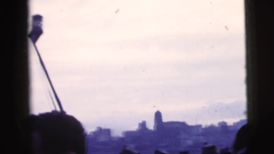 Late-1950s New York City river panorama with a silhouetted passenger, boat structure, and distant buildings under a pale sky.