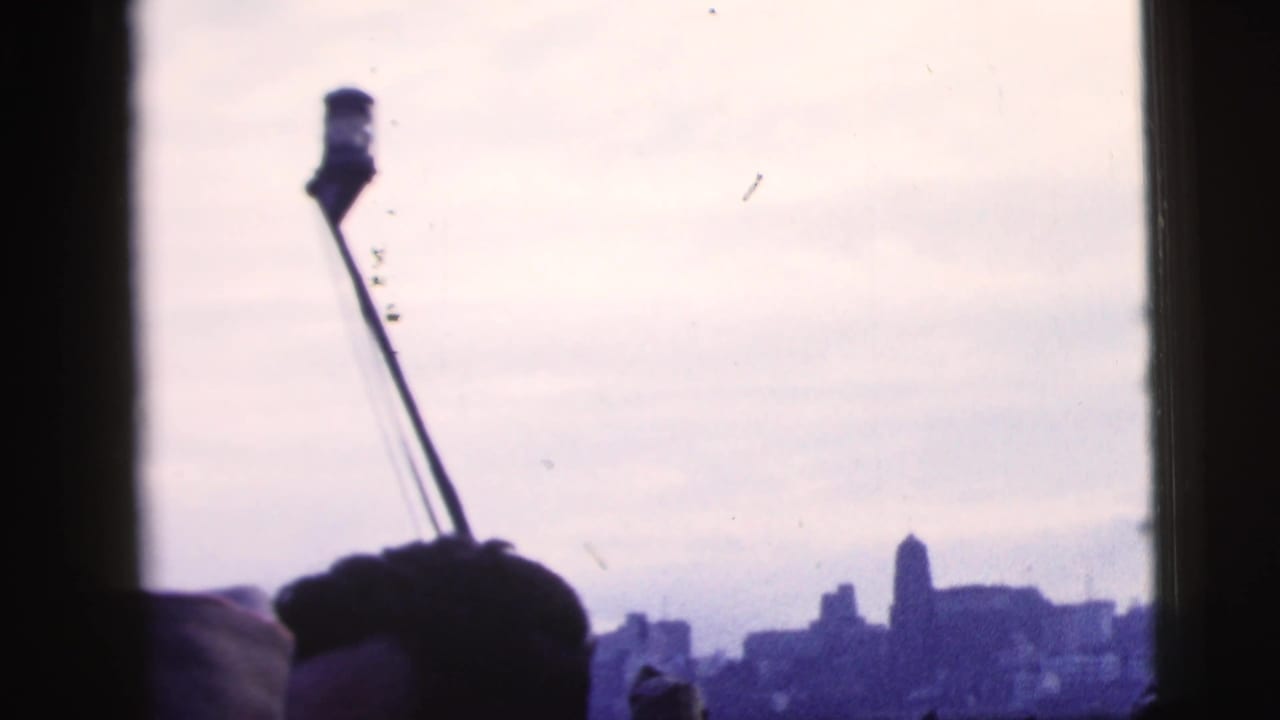 Silhouetted spectators and a slanted pole against a hazy waterfront skyline.