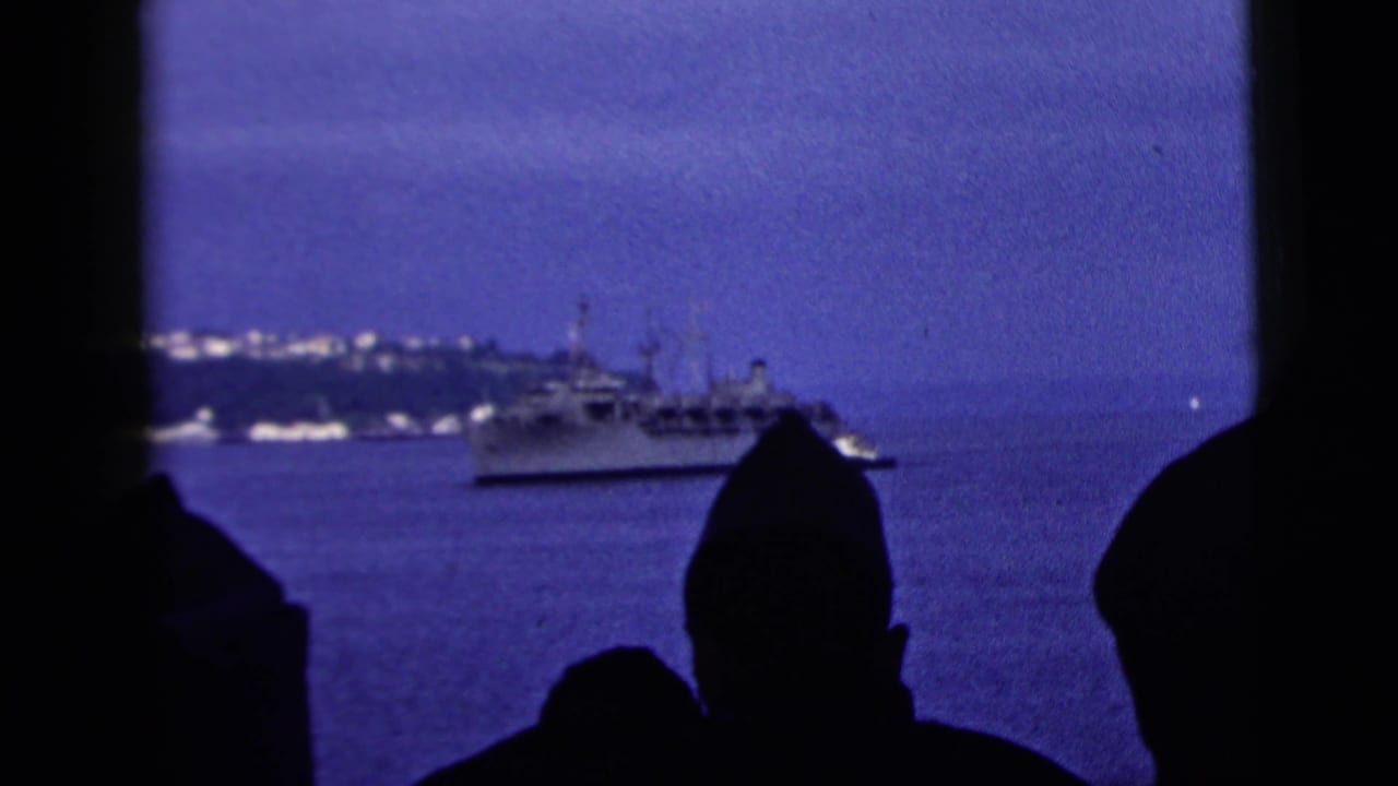 1958 New York City harbor view with silhouetted onlookers in the foreground and a vessel crossing the water near a distant shoreline.