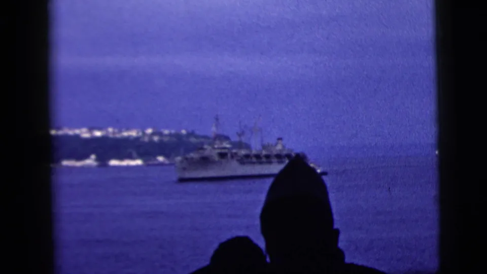 1958 New York City harbor footage with dark viewer silhouettes, a vessel offshore, and a softly lit skyline along the horizon.