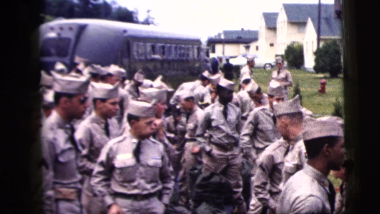 Uniformed men in grey clothing and pale caps stand near a bus and white buildings.