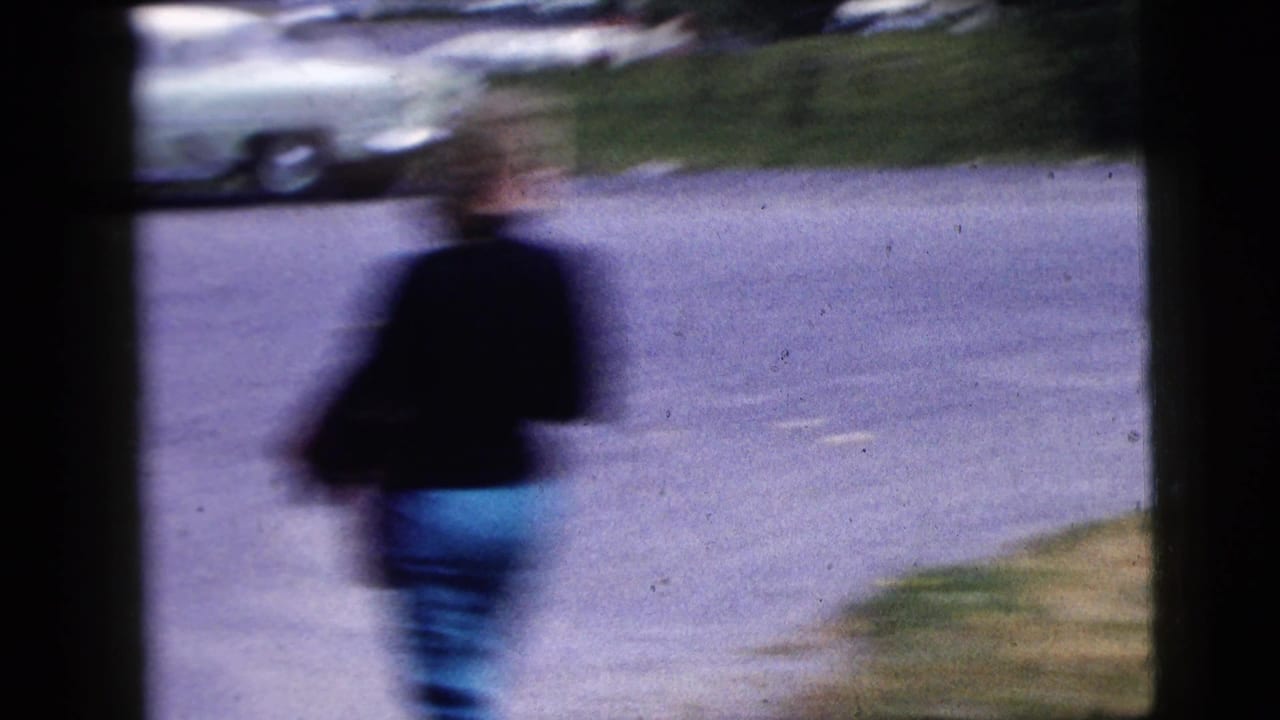 Blurred person walks along a road with a parked car in the background.