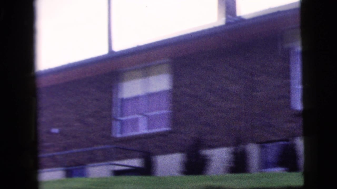 Brick building seen through dark window framing with bright sky above.