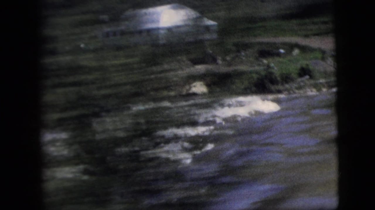 Blurred river bend with a pale building and dark shoreline.