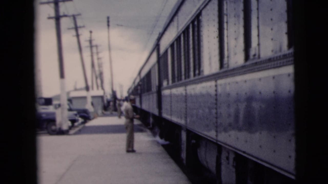 In the 1958 New York City footage, a man stands beside a vintage passenger train on a platform with utility poles and parked cars nearby.