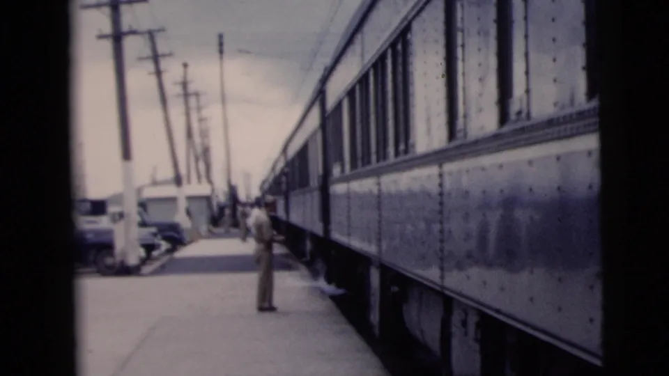 In the 1958 New York City footage, a man stands beside a vintage passenger train on a platform with utility poles and parked cars nearby.