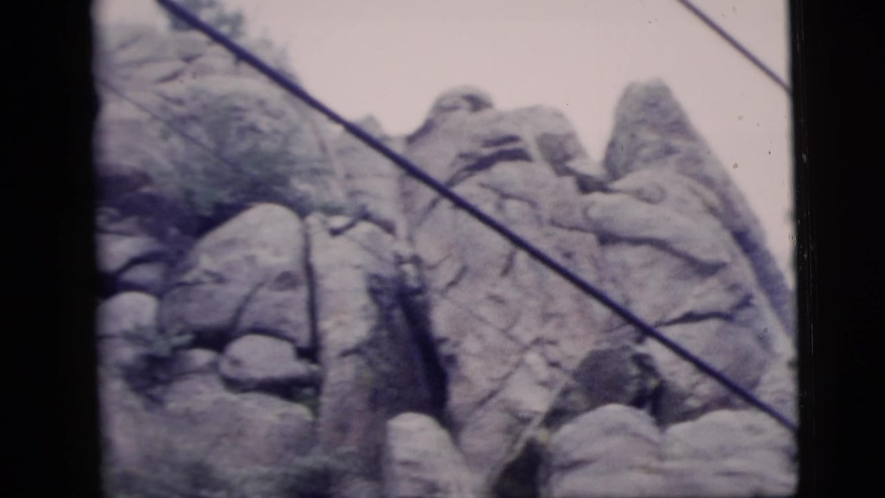 1958 8mm frame showing rugged rock formations with a diagonal cable crossing the view.