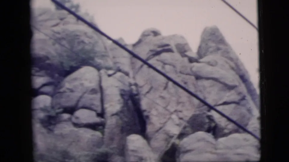 1958 8mm frame showing rugged rock formations with a diagonal cable crossing the view.